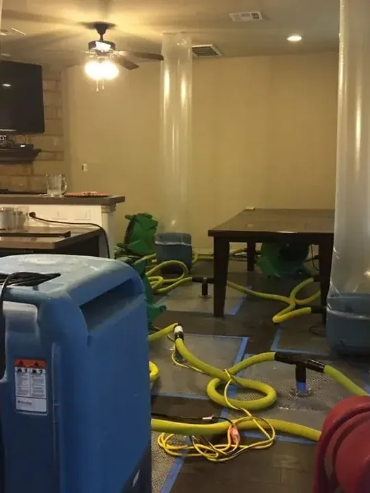 A blue dehumidifier and yellow drying hoses across a room floor