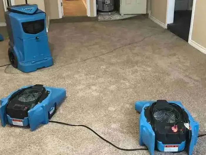 Blue air movers and a dehumidifier set on wet carpet