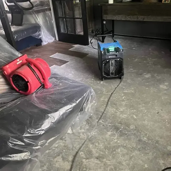 A red air mover and a dehumidifier in a room with plastic over the furniture