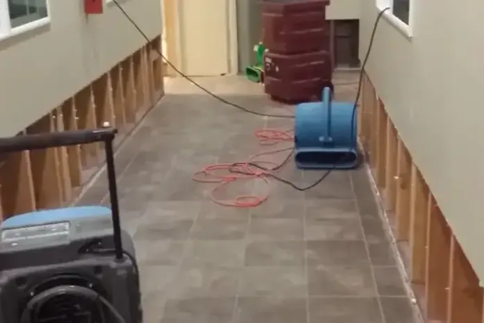 An air mover and dehumidifier drying a hallway after the lower drywall was cut away