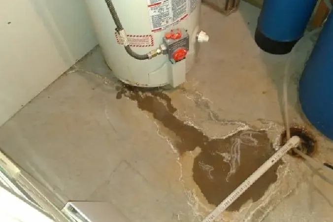A leaking water heater tank spreading rusty water over the floor